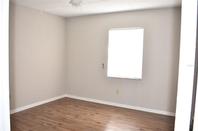 empty room with a textured ceiling, wood finished floors, a ceiling fan, and baseboards