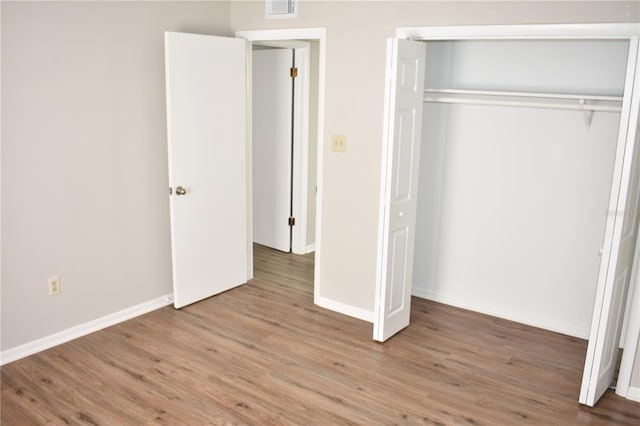 unfurnished bedroom featuring a closet, visible vents, baseboards, and wood finished floors