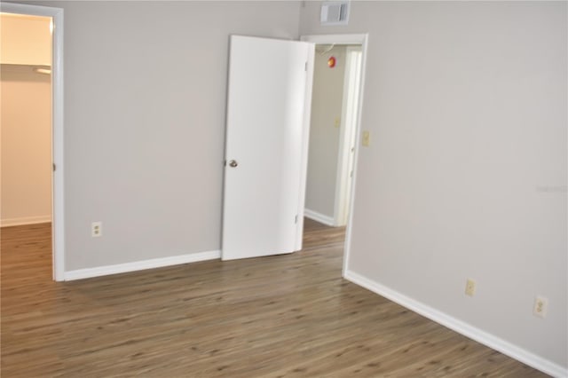 unfurnished bedroom with a walk in closet, visible vents, baseboards, and wood finished floors