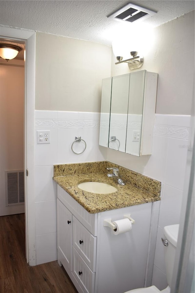 bathroom featuring visible vents, toilet, a textured ceiling, vanity, and wood finished floors