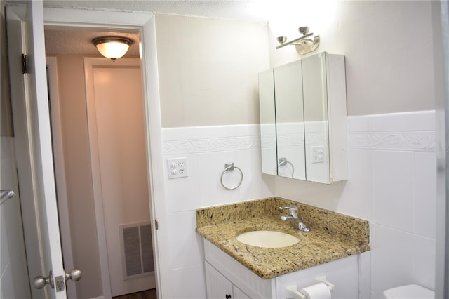 bathroom with a wainscoted wall, tile walls, visible vents, vanity, and a textured ceiling