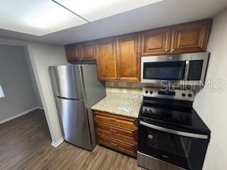 kitchen with light wood finished floors, baseboards, appliances with stainless steel finishes, and brown cabinetry