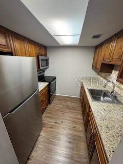 kitchen with backsplash, appliances with stainless steel finishes, light wood-style floors, brown cabinetry, and a sink