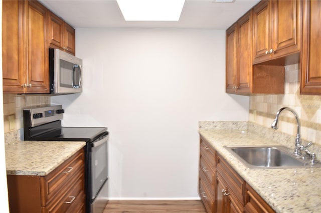 kitchen featuring stainless steel appliances, a skylight, brown cabinetry, and a sink