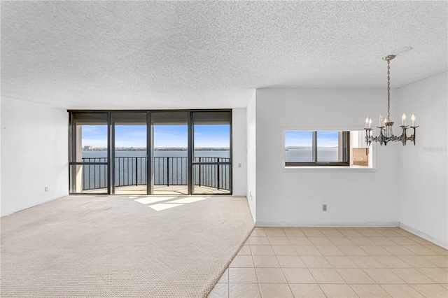 spare room featuring a water view, floor to ceiling windows, carpet floors, a notable chandelier, and a textured ceiling