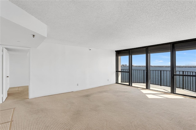 carpeted empty room with a wall of windows, a water view, a textured ceiling, and a healthy amount of sunlight