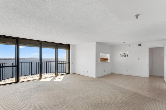 empty room featuring light tile patterned flooring, floor to ceiling windows, a textured ceiling, light carpet, and a notable chandelier