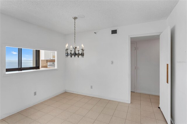 spare room with visible vents, a notable chandelier, a textured ceiling, light tile patterned floors, and baseboards