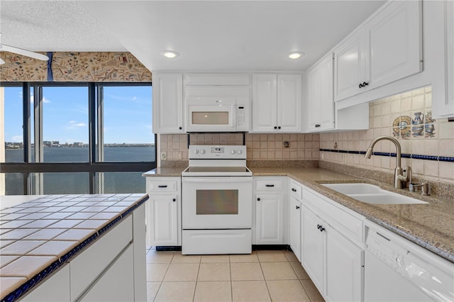 kitchen with a sink, white appliances, tile counters, and white cabinets