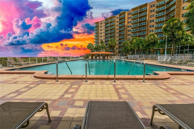 pool at dusk featuring a patio area, a community pool, and fence