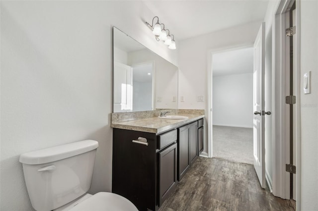 half bath with toilet, wood finished floors, and vanity