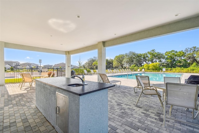 view of patio with a community pool, fence, outdoor dry bar, and a sink