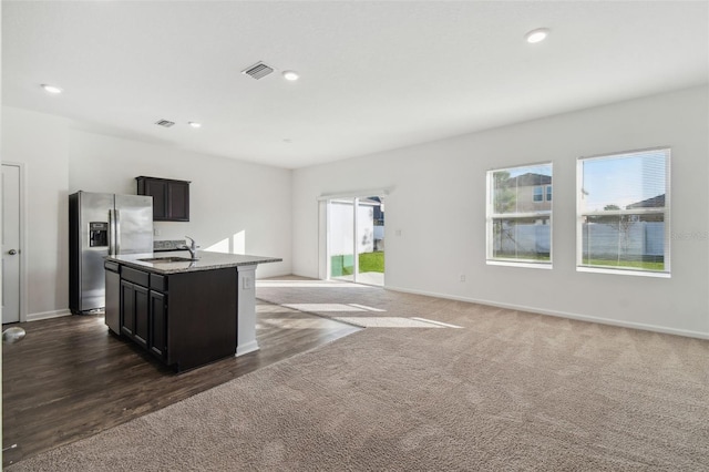 kitchen featuring a sink, visible vents, stainless steel fridge with ice dispenser, dark colored carpet, and a center island with sink