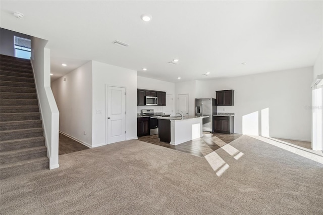 kitchen featuring stainless steel appliances, carpet floors, open floor plan, light countertops, and an island with sink