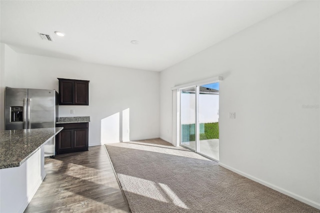 kitchen featuring visible vents, dark wood finished floors, dark stone counters, stainless steel fridge with ice dispenser, and dark brown cabinets