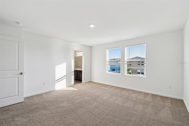 unfurnished bedroom with baseboards, ensuite bath, and light colored carpet