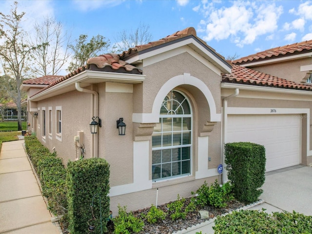 view of property exterior with a tiled roof, an attached garage, and stucco siding