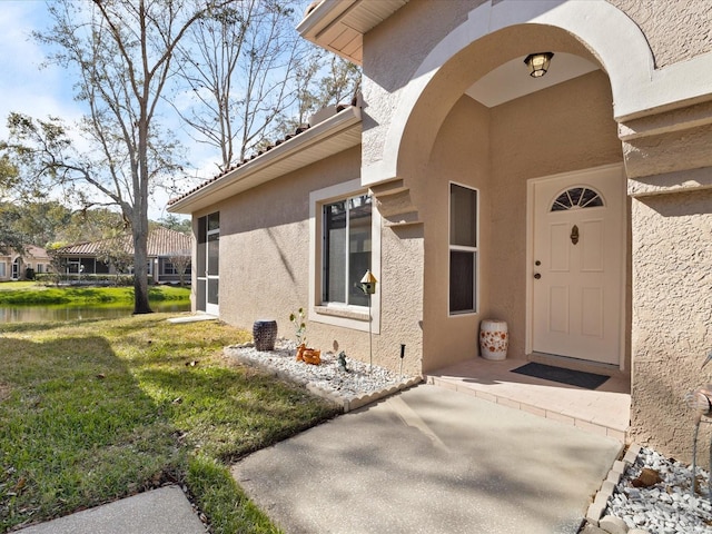 doorway to property featuring a water view, a yard, and stucco siding