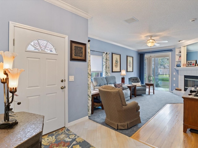 foyer with a textured ceiling, a tiled fireplace, visible vents, and crown molding