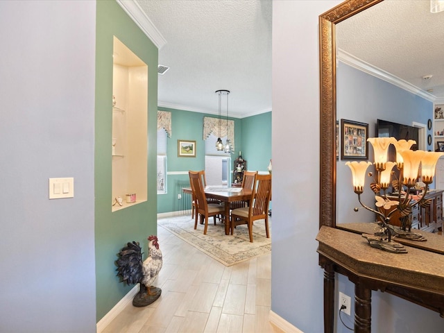 hall featuring light wood-type flooring, ornamental molding, and a textured ceiling