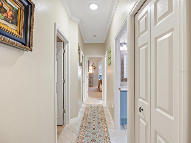 corridor with ornamental molding, light tile patterned flooring, and baseboards