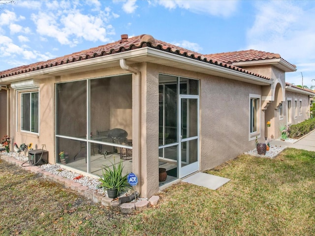 view of property exterior featuring a tile roof, a sunroom, and stucco siding