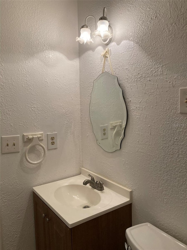 half bath featuring toilet, a textured wall, and vanity