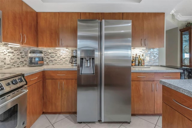 kitchen with light tile patterned floors, appliances with stainless steel finishes, backsplash, and brown cabinets