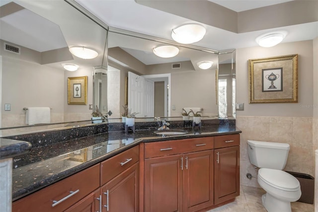 bathroom featuring visible vents, toilet, tile patterned floors, vanity, and tile walls