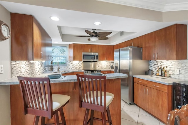 kitchen featuring a ceiling fan, a sink, a raised ceiling, backsplash, and appliances with stainless steel finishes