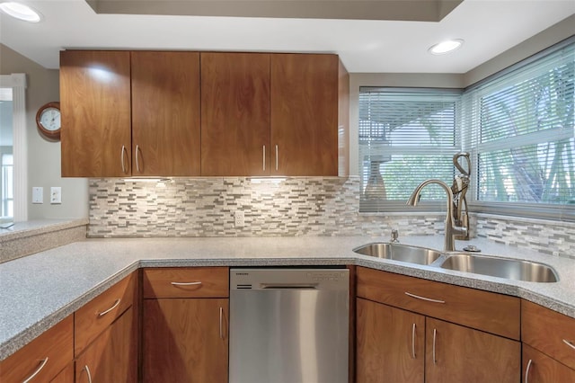 kitchen with stainless steel dishwasher, a sink, brown cabinets, light countertops, and backsplash
