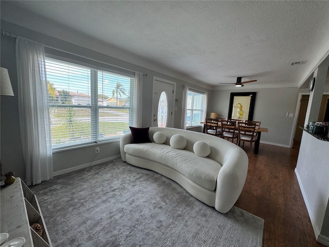 living room with a textured ceiling, a wealth of natural light, dark wood-style flooring, and visible vents