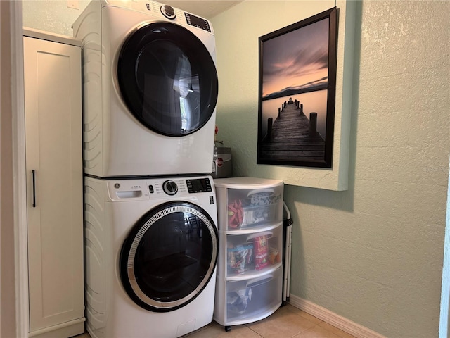 laundry room with light tile patterned floors, a textured wall, laundry area, baseboards, and stacked washer / drying machine