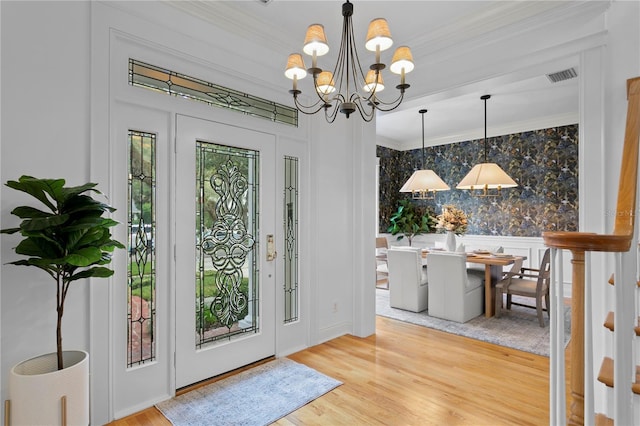 doorway featuring wallpapered walls, visible vents, wood finished floors, an inviting chandelier, and crown molding