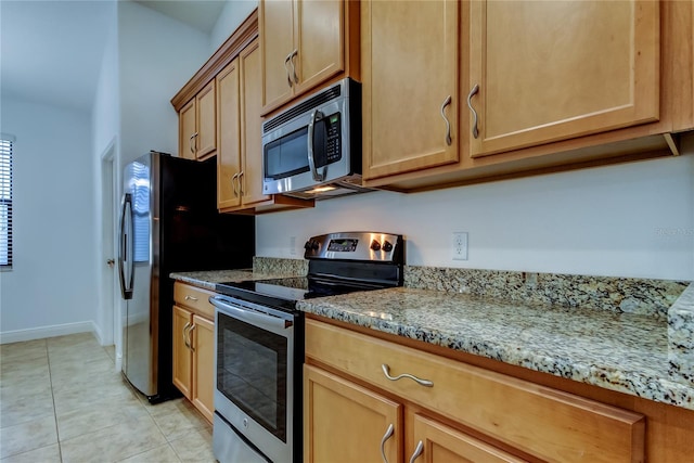 kitchen featuring light tile patterned floors, stainless steel appliances, light stone counters, and baseboards