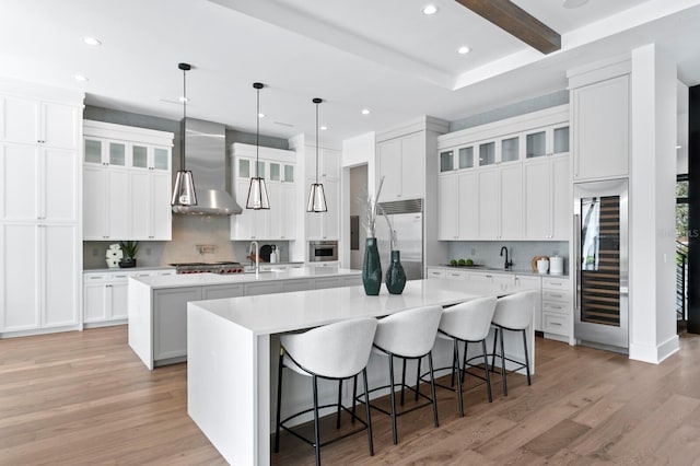 kitchen featuring a spacious island, light countertops, appliances with stainless steel finishes, wall chimney exhaust hood, and light wood finished floors
