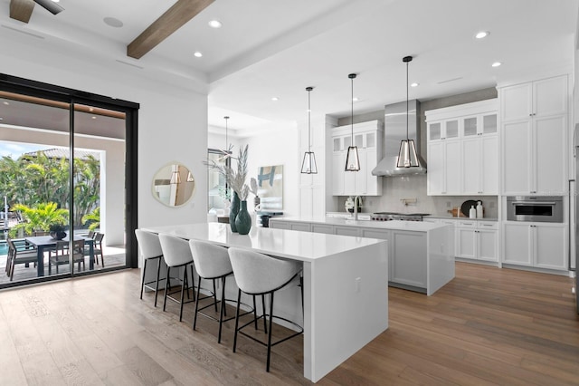 kitchen featuring white cabinets, decorative backsplash, a spacious island, wood finished floors, and wall chimney range hood