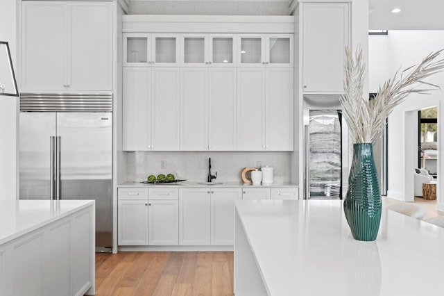 kitchen with white cabinets, stainless steel built in fridge, light countertops, and light wood-style floors