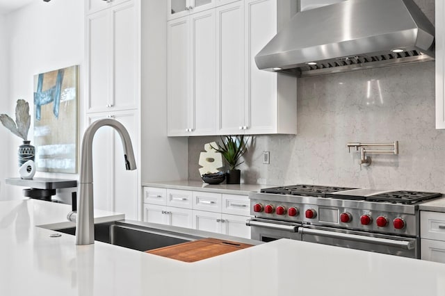 kitchen featuring tasteful backsplash, range with two ovens, wall chimney exhaust hood, glass insert cabinets, and white cabinetry
