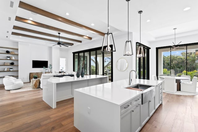 kitchen with beamed ceiling, hardwood / wood-style floors, an island with sink, and a sink