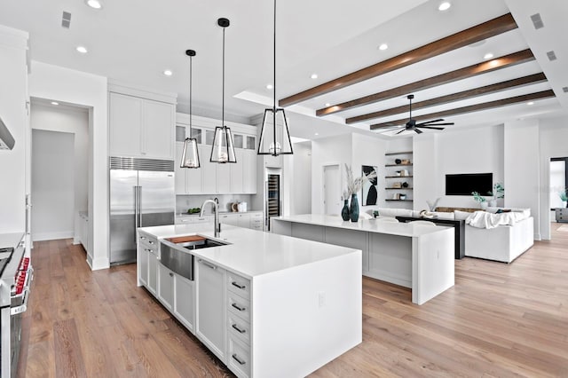 kitchen with light wood-style flooring, a sink, high quality appliances, white cabinetry, and a center island with sink