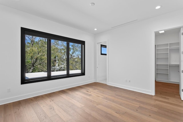 unfurnished bedroom featuring light wood-style floors, a spacious closet, baseboards, and recessed lighting