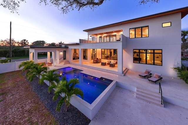 rear view of house featuring a fenced in pool, a patio area, a balcony, and stucco siding