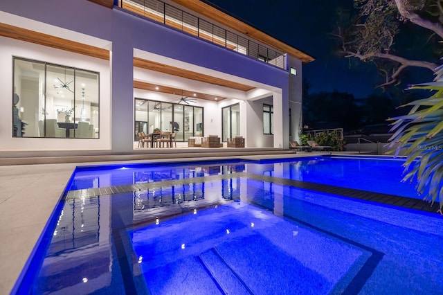 pool at night featuring a patio area, ceiling fan, an outdoor pool, and an in ground hot tub