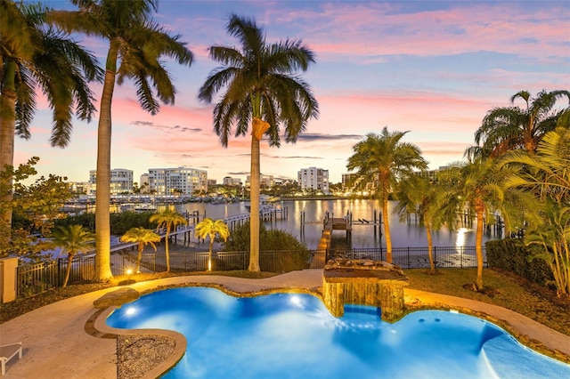 view of swimming pool featuring a water view, fence, a fenced in pool, a view of city, and a dock