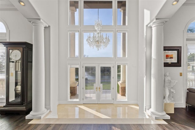 doorway with a towering ceiling, ornate columns, wood finished floors, and an inviting chandelier