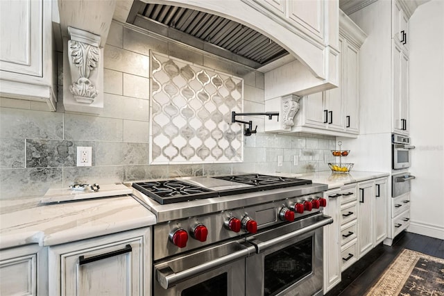 kitchen featuring dark wood-style flooring, a warming drawer, stainless steel appliances, decorative backsplash, and premium range hood