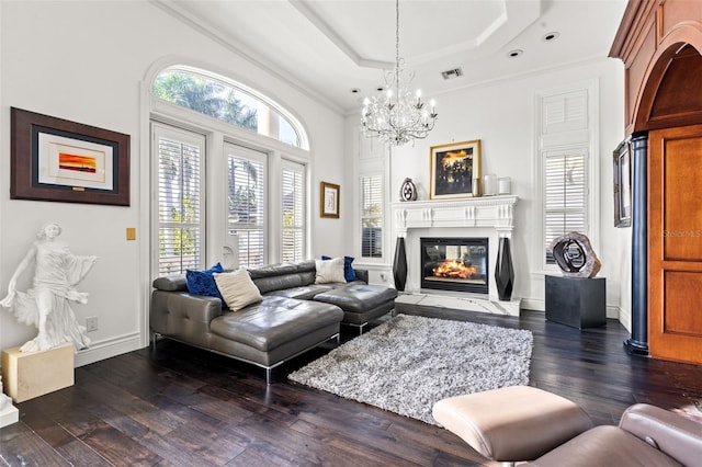 living area featuring a tray ceiling, dark wood finished floors, visible vents, a glass covered fireplace, and baseboards