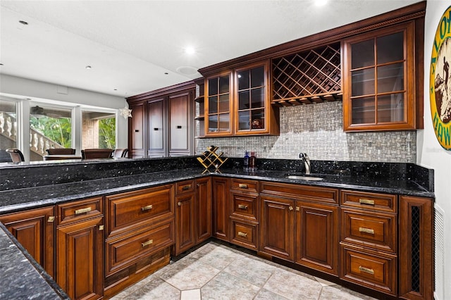 kitchen featuring glass insert cabinets, dark stone counters, a sink, and decorative backsplash