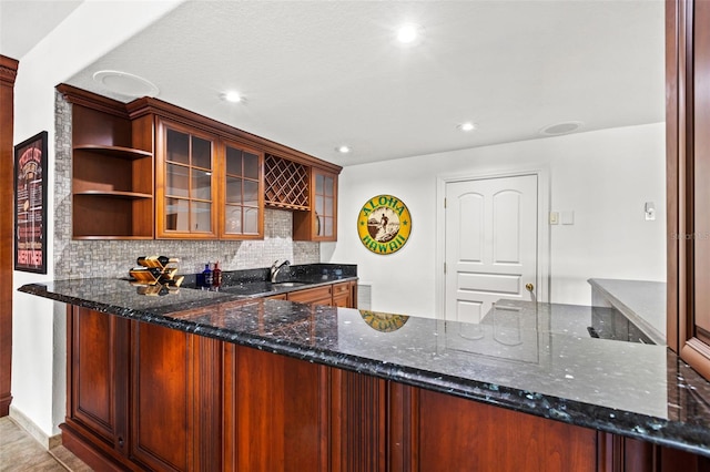 kitchen with dark stone counters, a peninsula, open shelves, and backsplash